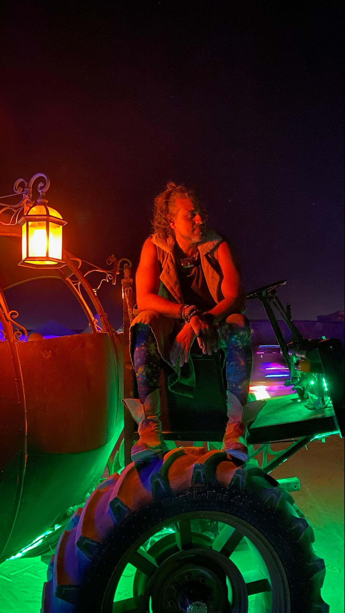Man seated in a surreal nighttime setting lit by neon colors and lanterns — relaxed, otherworldly, creative energy.