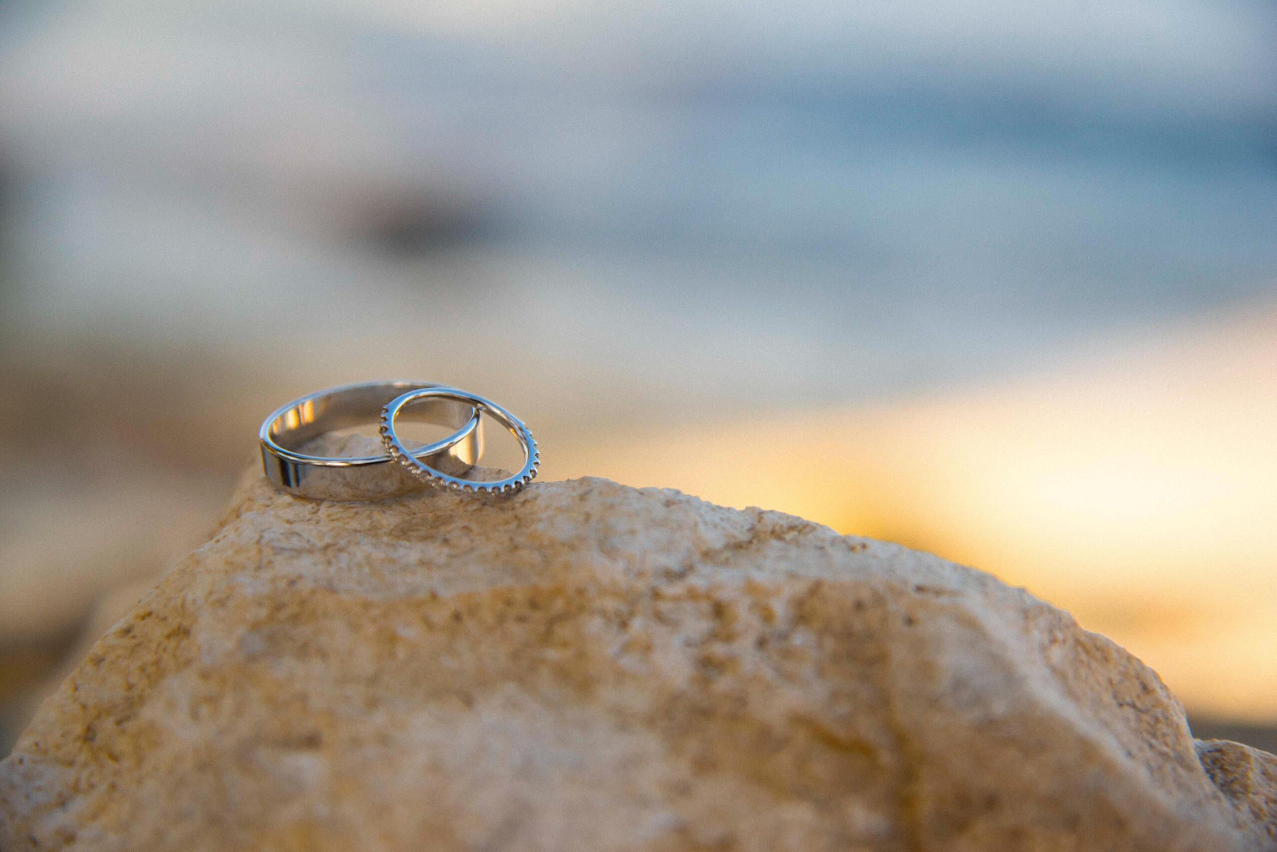 Two wedding rings resting on a smooth stone, captured with a shallow depth of field at golden hour — simple, poetic, symbolic of union.