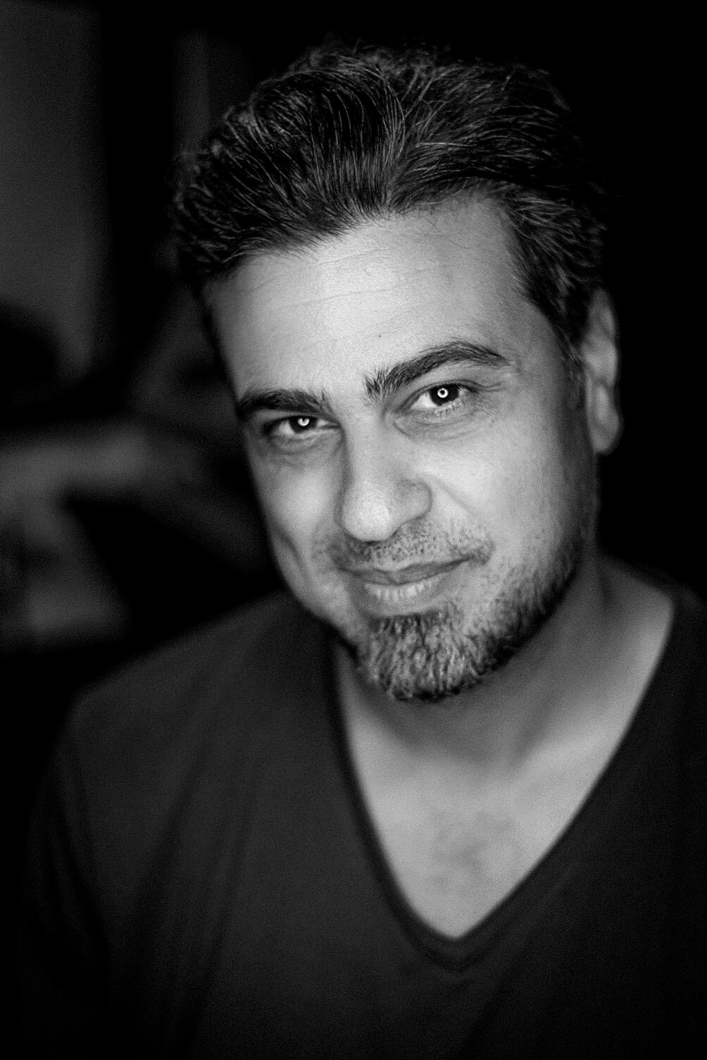 Black and white headshot of photographer Arash Afshar, wearing a relaxed expression and soft lighting — authentic, grounded presence.